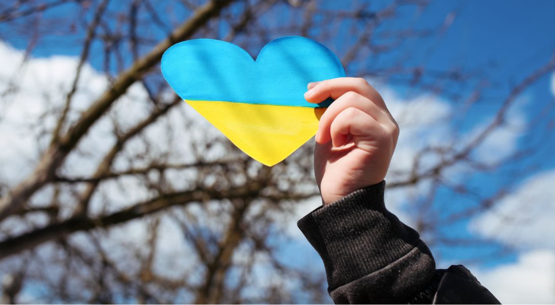 A blue and yellow paper heart, being held by a hand.